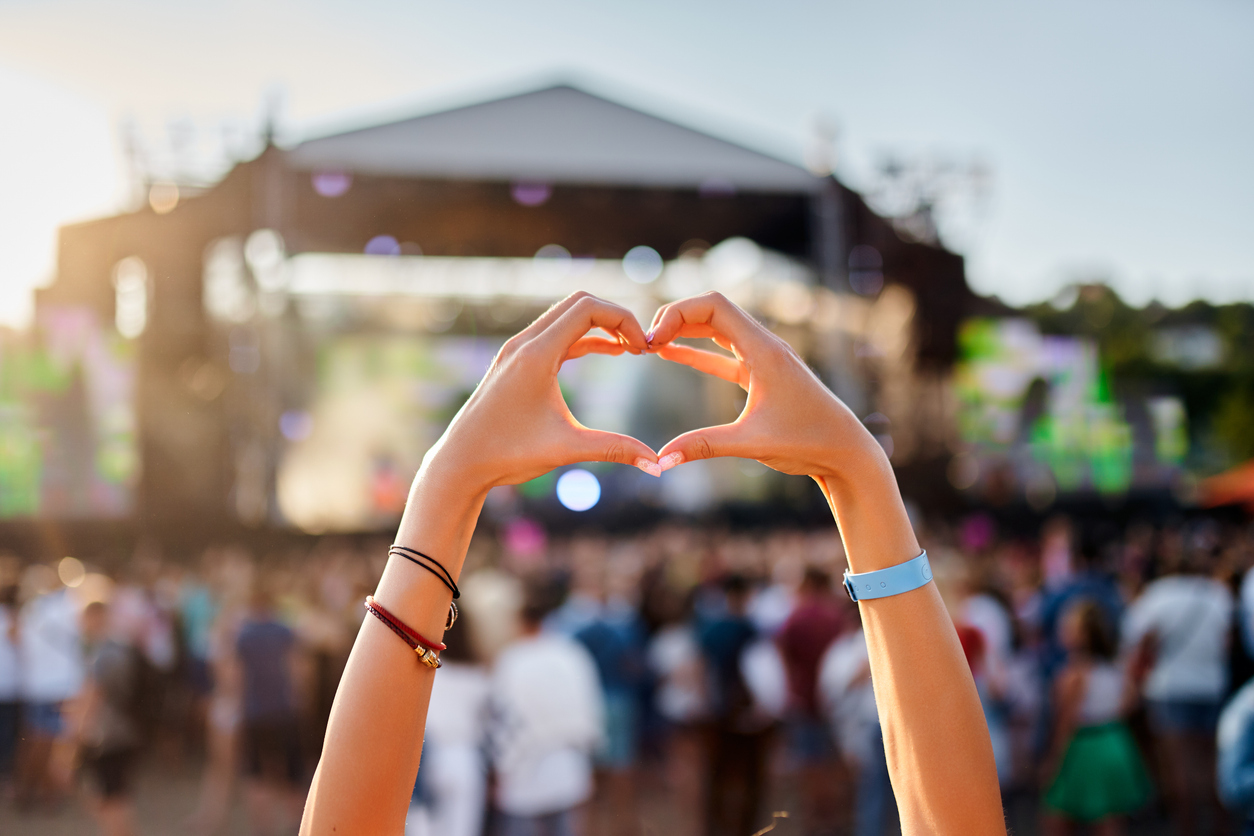 Festivalgoers form a heart with their hands in front of a concert stage at sunset