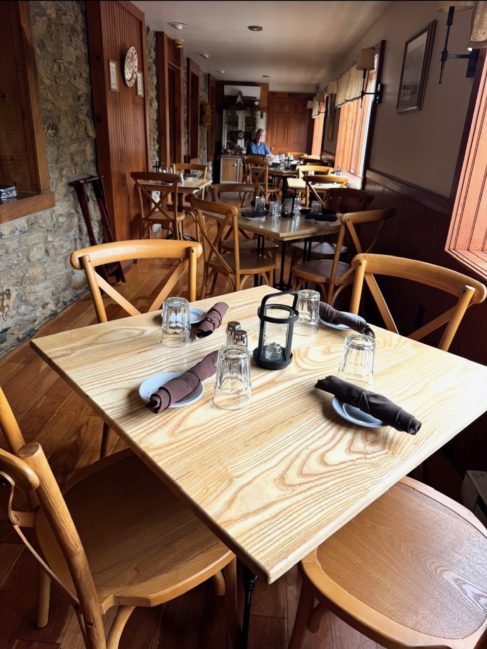 A bare ash dining table set with napkins and glassware in the Limeport Inn dining room, with Mark Jamison in the background.