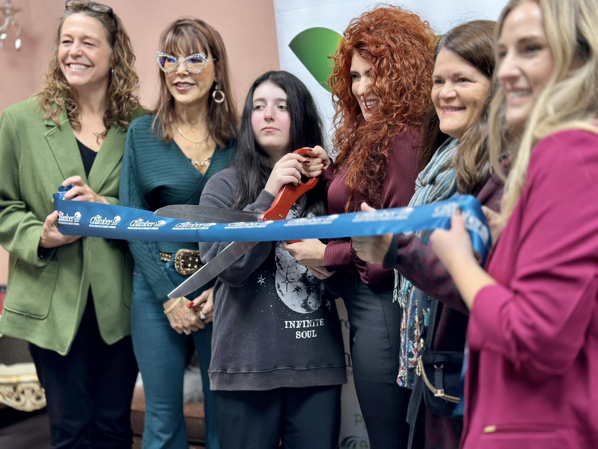 Michelle and a group of women holding a blue Greater Lehigh Valley Chamber of Commerce ribbon as it is cut with oversized ceremonial scissors.
