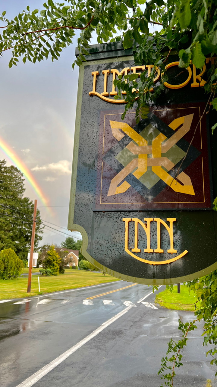 The Limeport Inn sign beside a wet road, with a rainbow in the sky behind it.