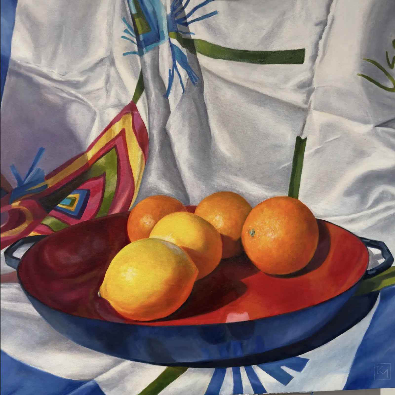 Oil painting of lemons and oranges in a red enamel pan resting on draped white, blue and magenta patterned scarves.