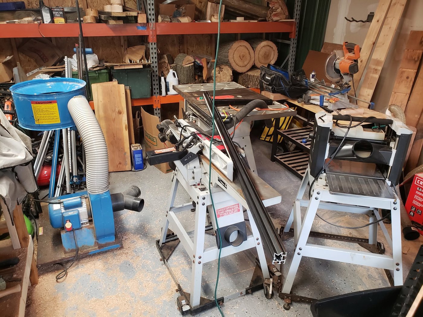 A woodworking shop with a table saw, planer, dust collector and racks of lumber.