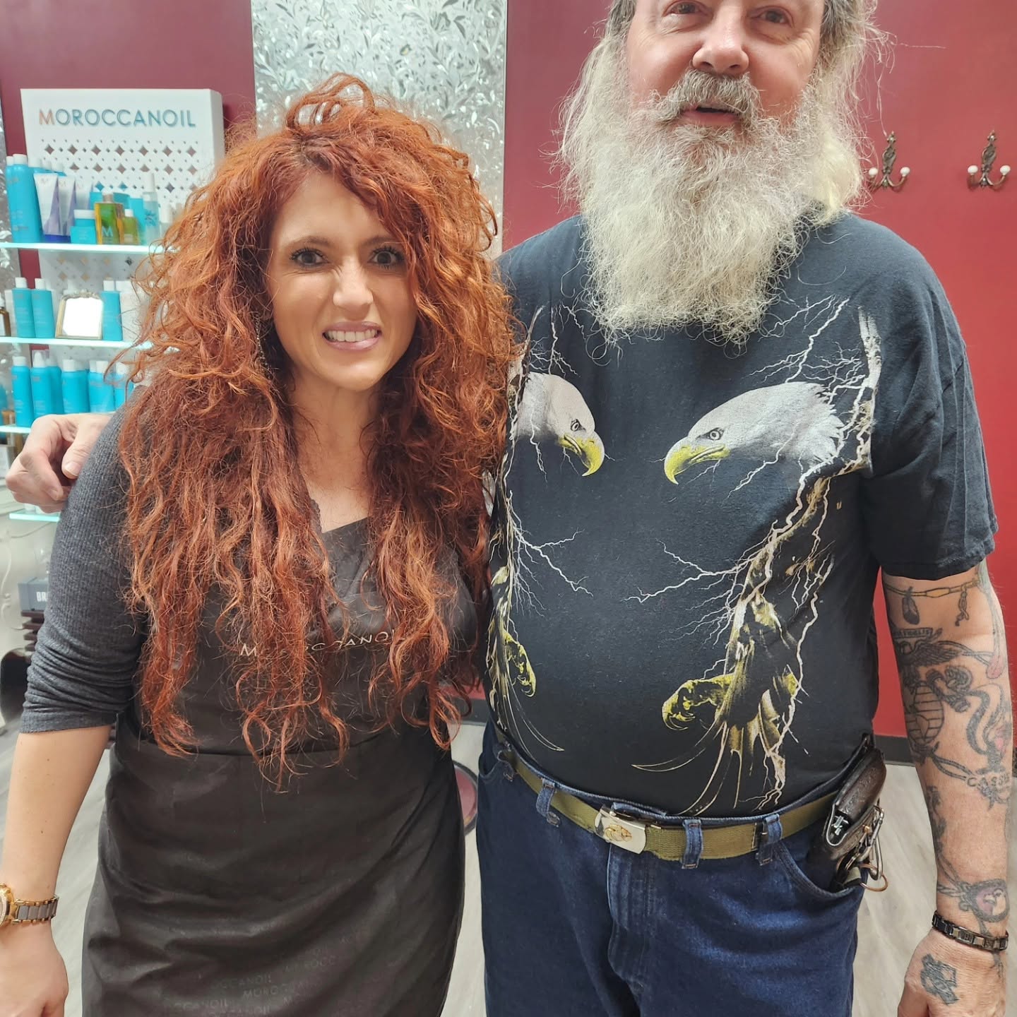 Michelle, in a Moroccanoil apron, standing with a bearded client in the salon.