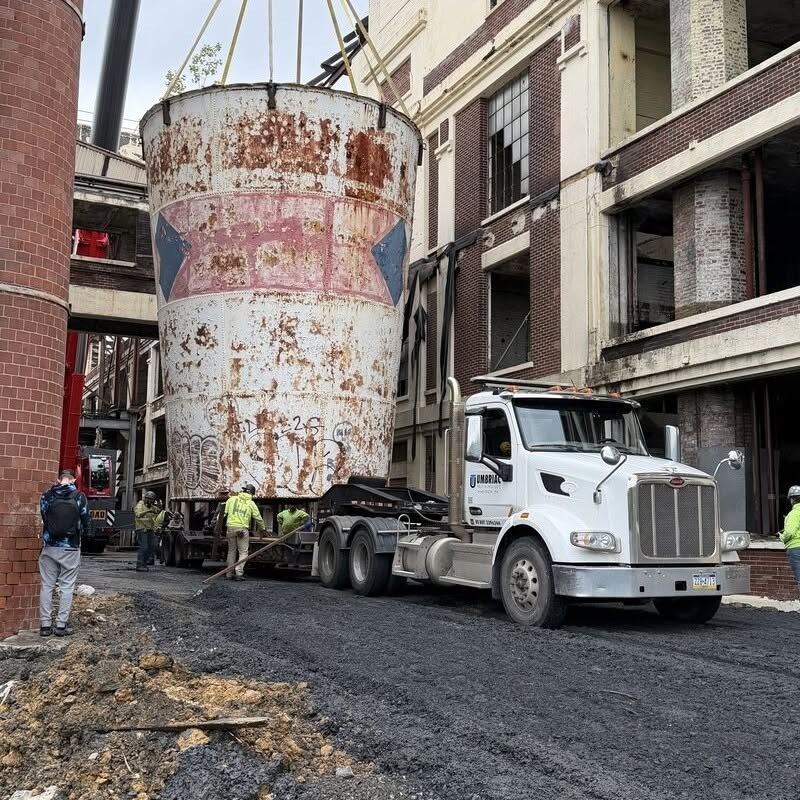The rusted 50,000-gallon Dixie Cup water tower loaded on a flatbed truck beside the factory after being lowered