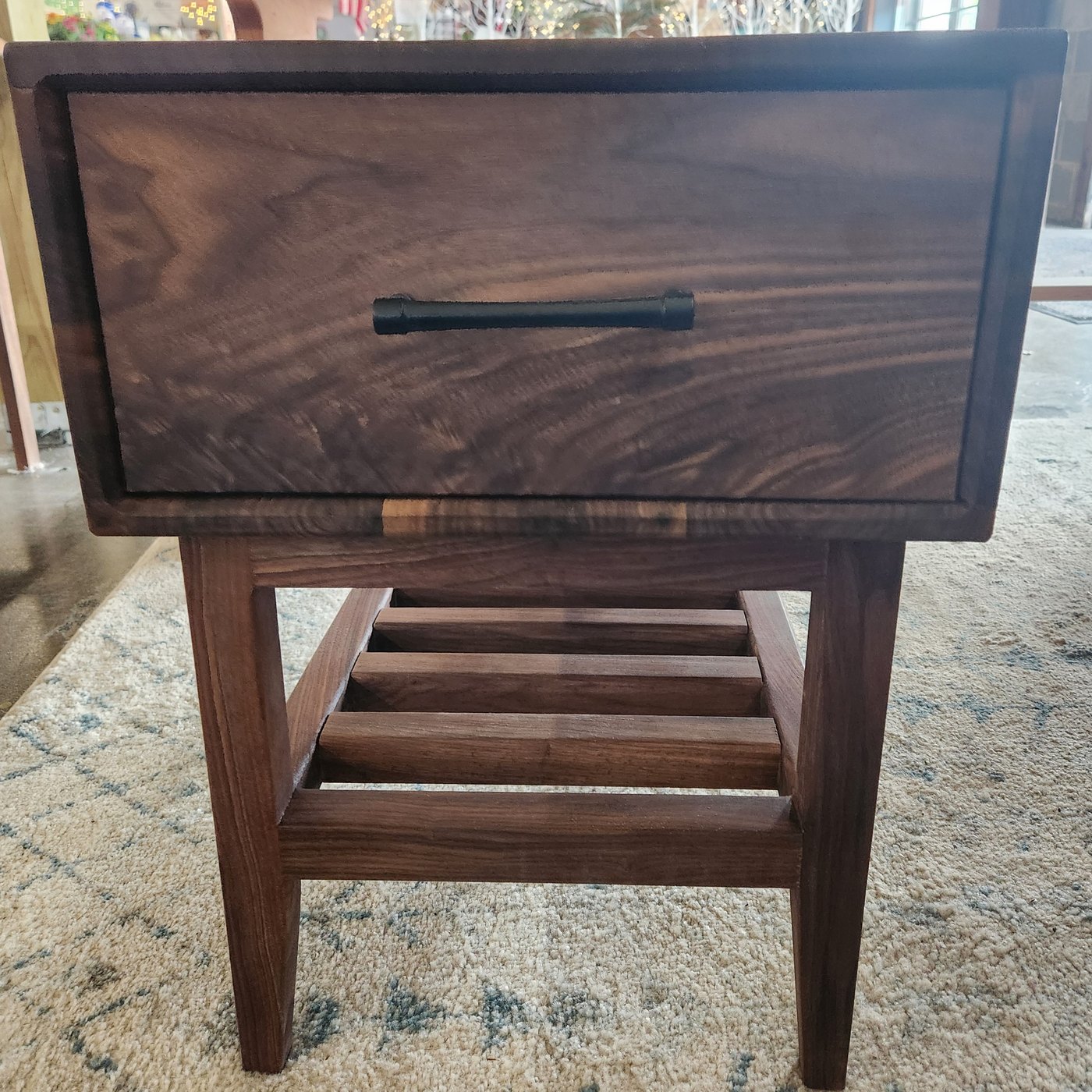 A dark hardwood nightstand with a single drawer and a slatted lower shelf.