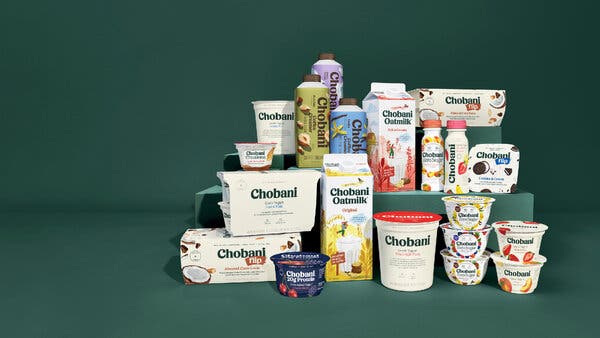 An assortment of Chobani products, including Greek yogurt cups and tubs, Flip snack cups, oat milk cartons and bottled coffee creamers, arranged on green steps.