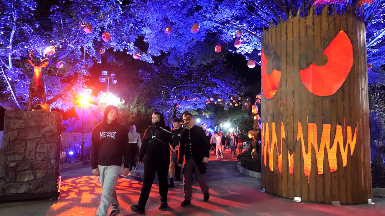 Visitors walking a Dorney Park path at night past a wooden jack-o-lantern facade with glowing eyes