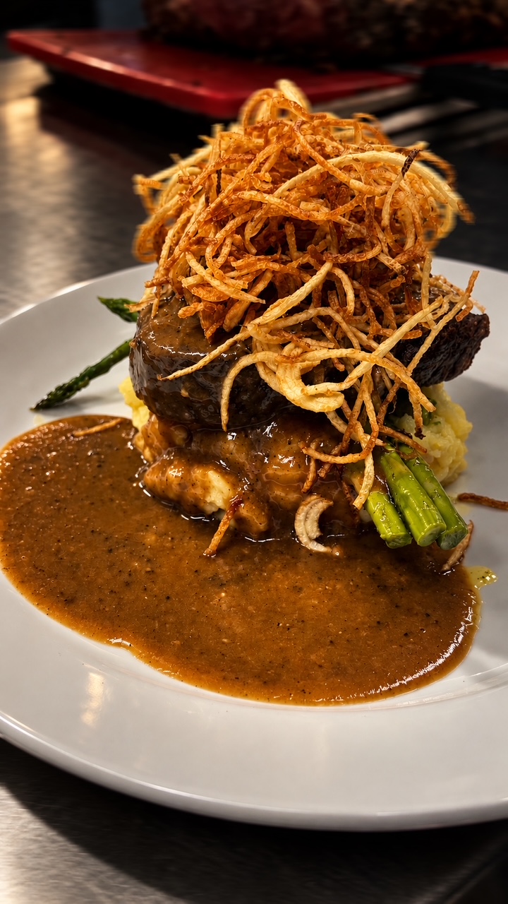 A plated steak on mashed potatoes with asparagus, pan sauce and crispy frizzled onions.
