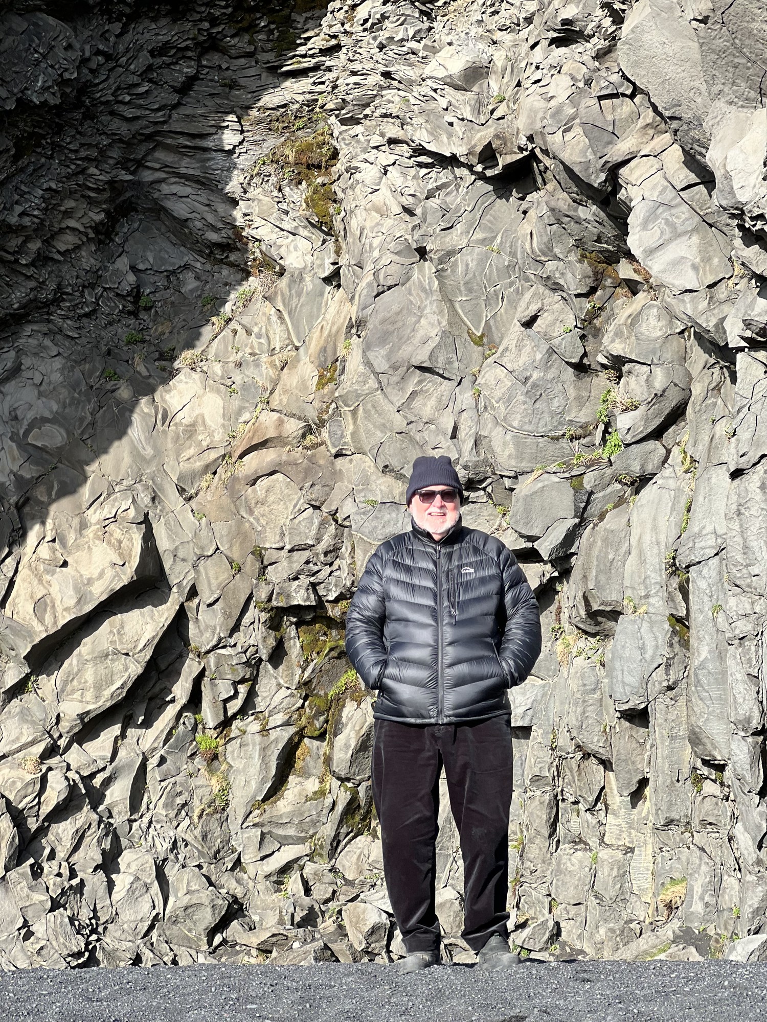 Eugene Sheedy standing before towering basalt cliffs while traveling