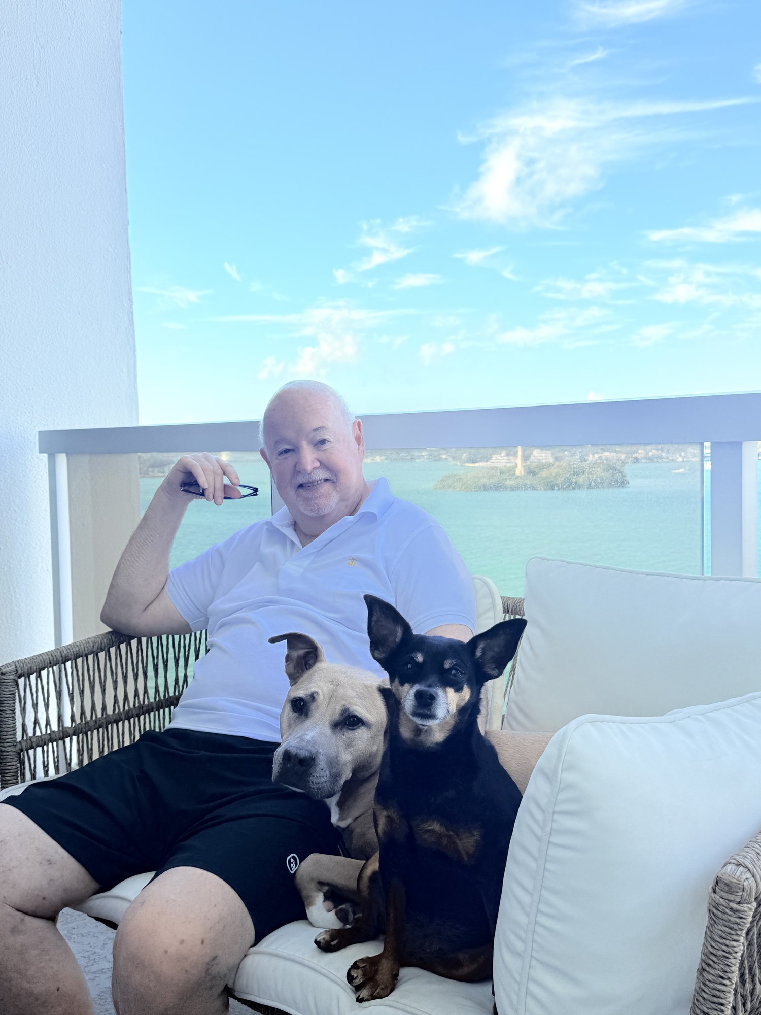 Eugene Sheedy seated with his two rescue dogs on a balcony overlooking the water