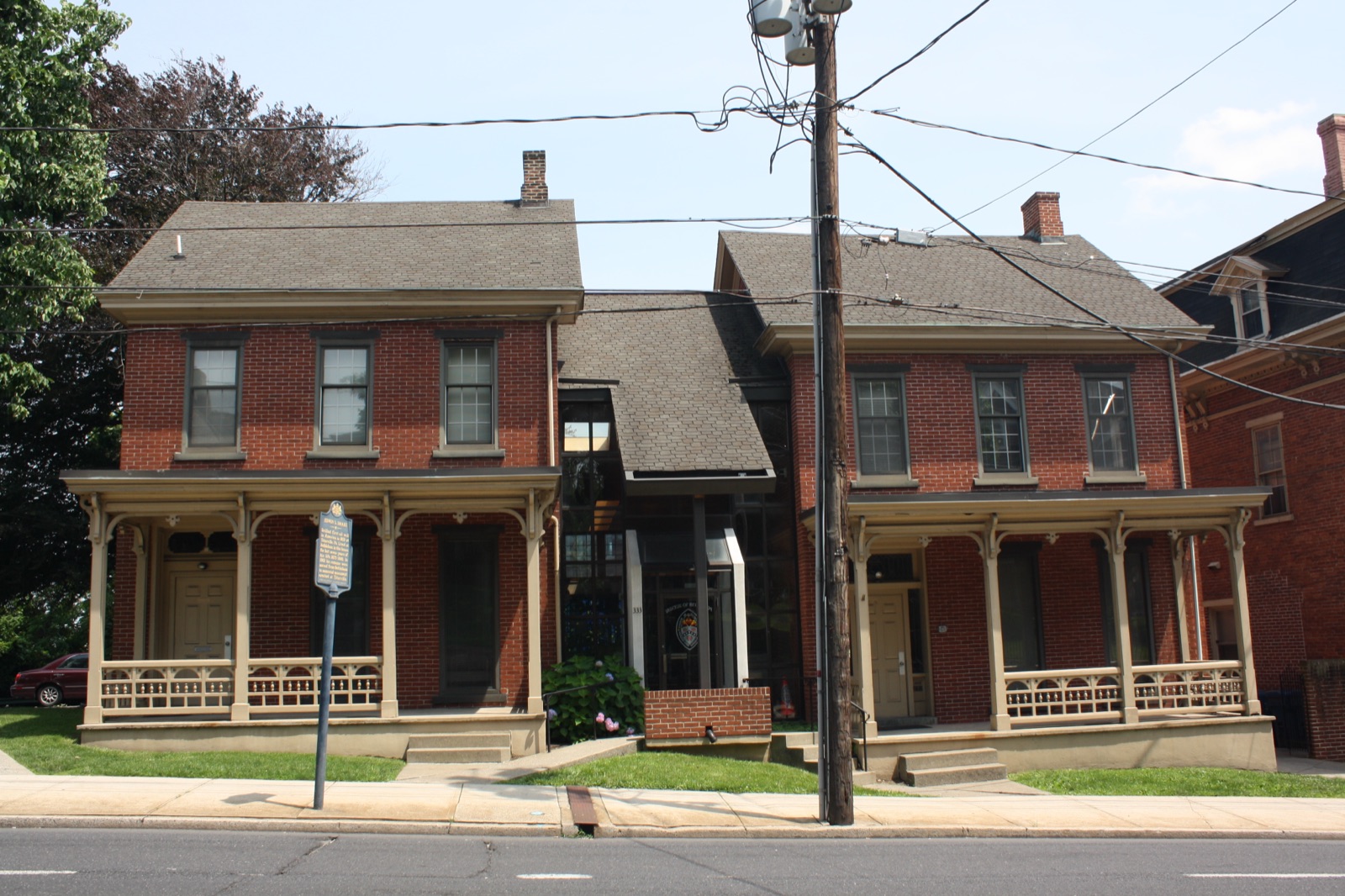 The Edwin Drake House, a modest two-story brick twin with a bracketed porch and a state historical marker in front