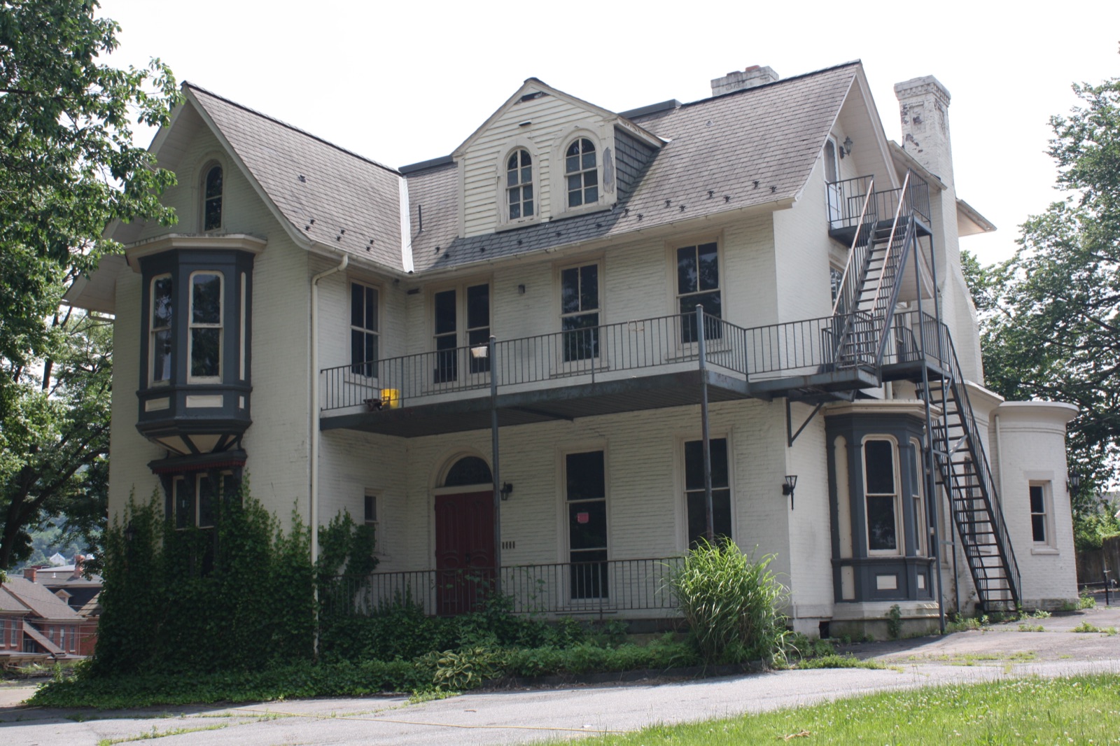 The William Sayre Mansion, vacant, with ivy growing into the painted brick and a steel fire escape across the front