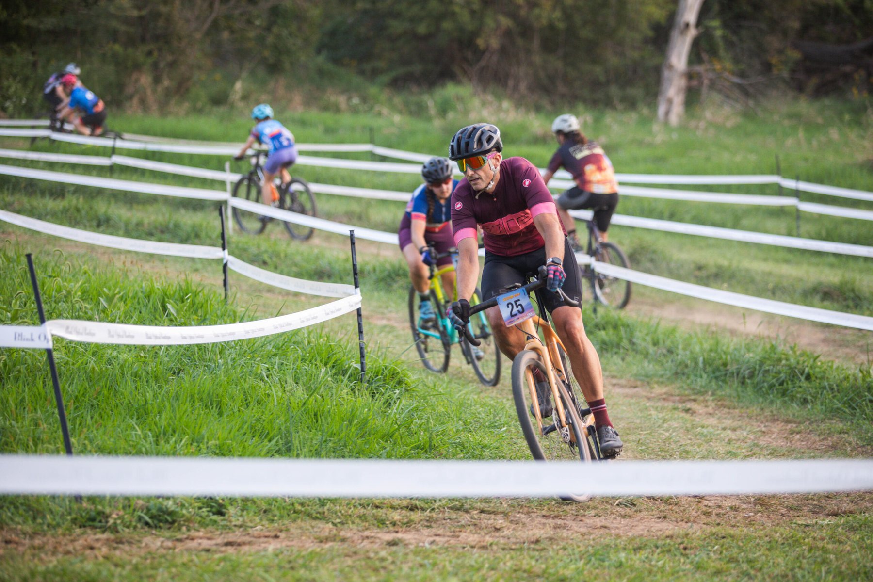 Cyclocross riders follow a taped, winding course through the grass at Fifth Street Cross