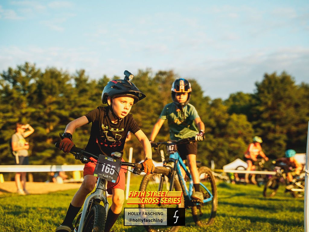 A young racer in a Kitli jersey leads adult riders on the course