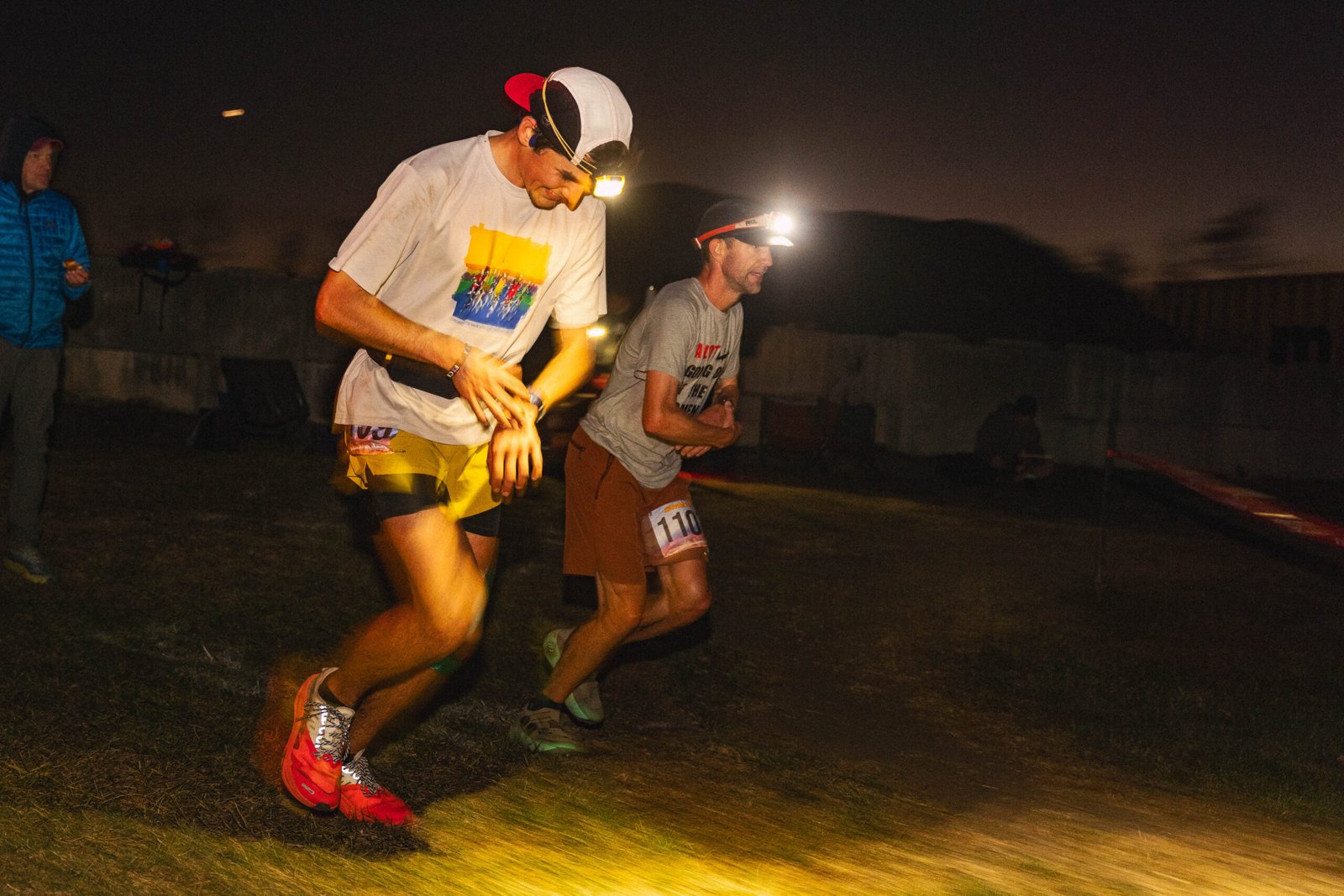 Two runners wearing headlamps check their watches during a night race
