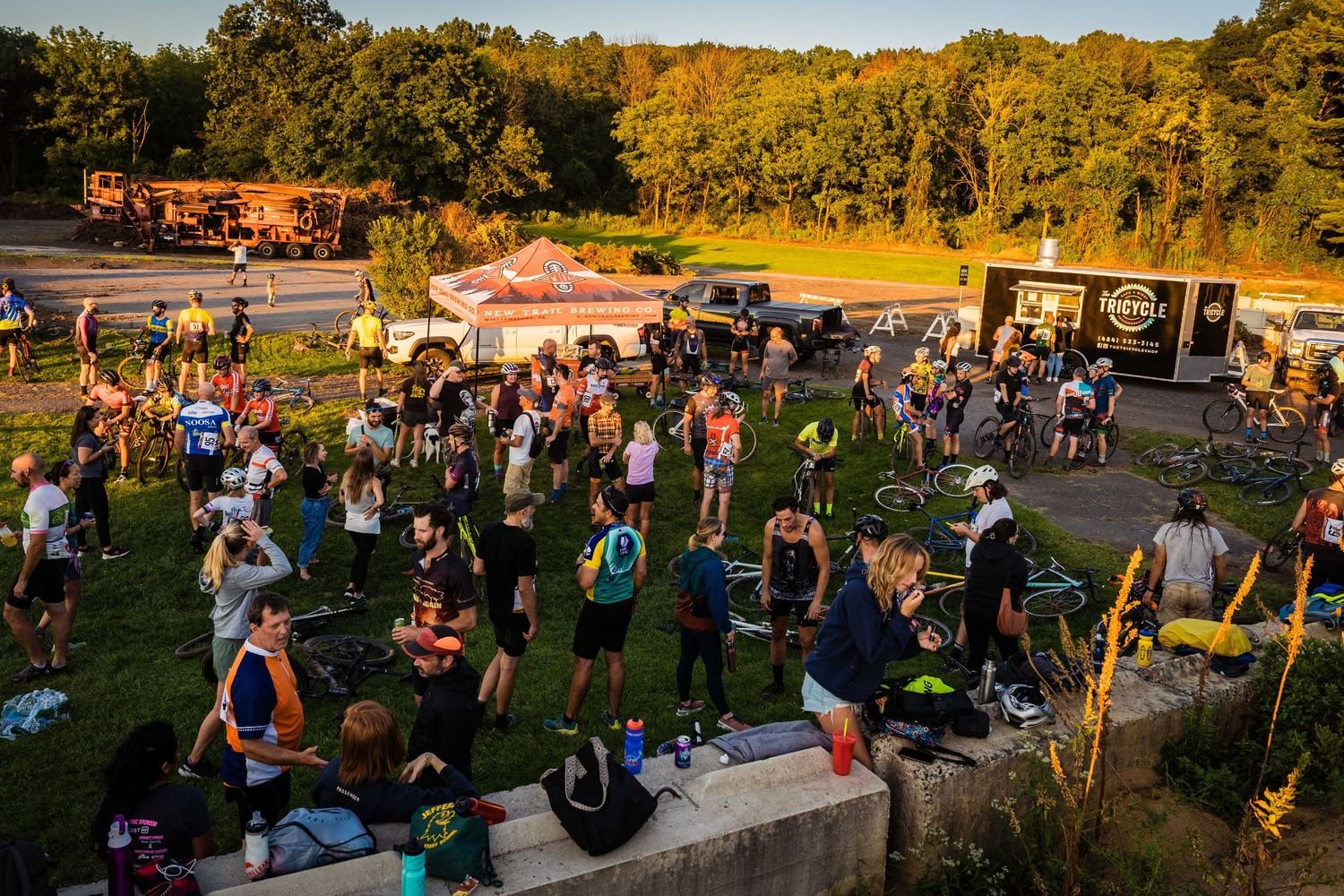 A crowd of racers, bikes and friends on the grass at the Emmaus Compost Center, with a brewery tent and food truck