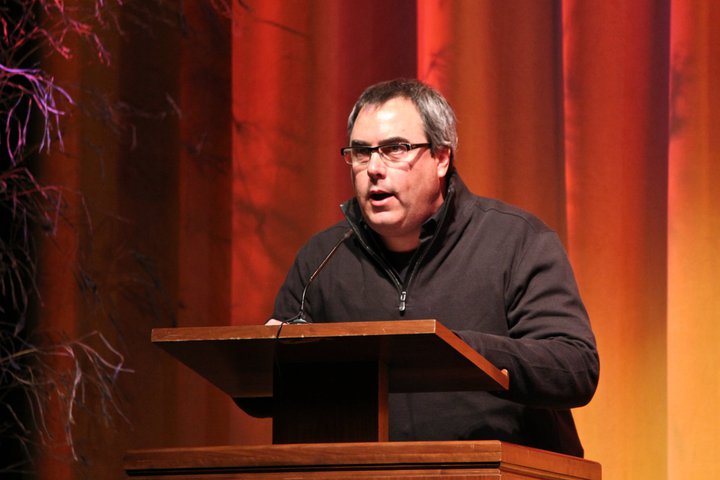 Matt Metal presenting at the Lehigh Valley Music Awards, speaking at a wooden podium in front of a red stage curtain at the Scottish Rite Cathedral in Allentown