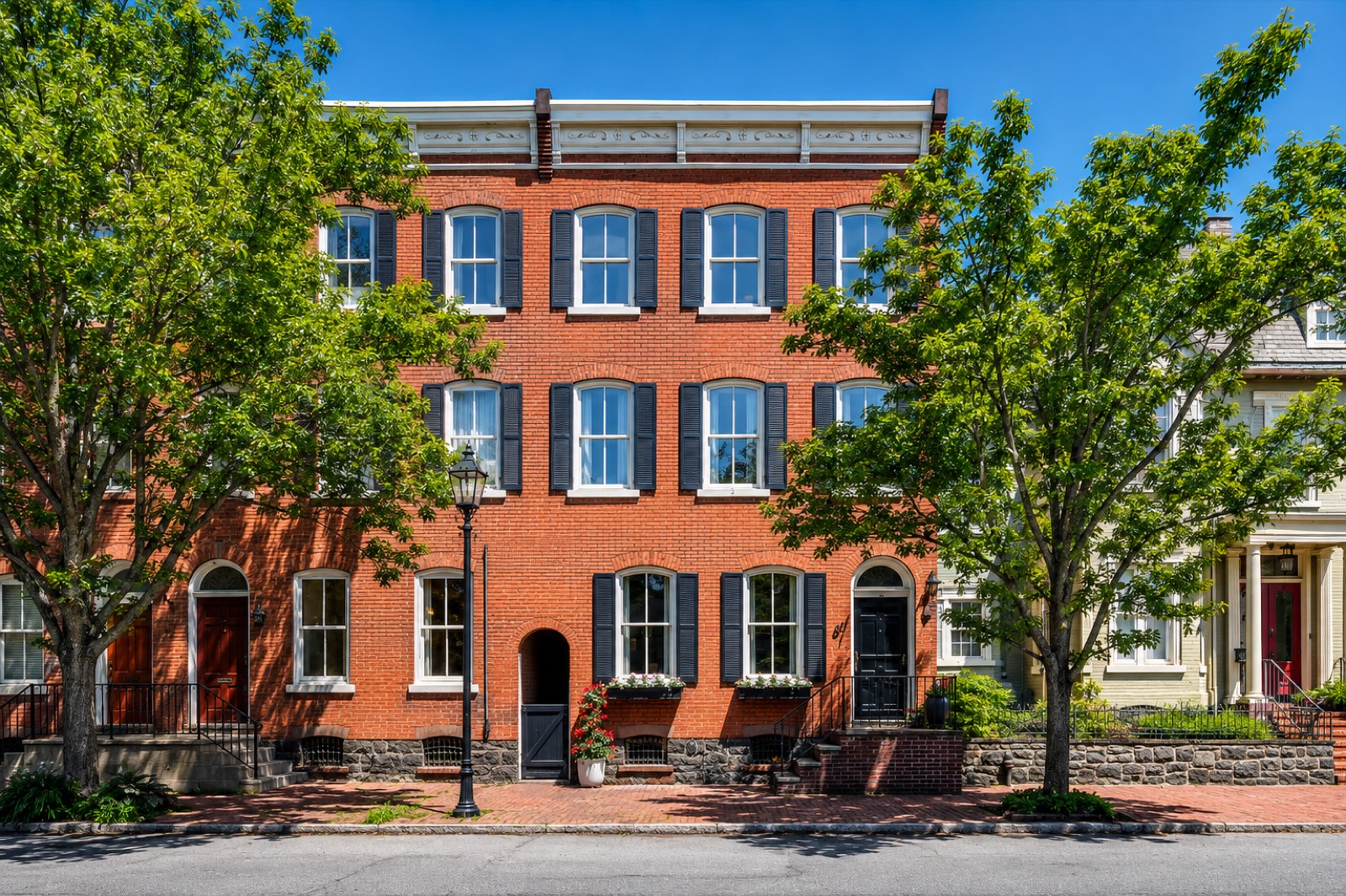 Three-storey red brick rowhouses with black shutters, arched doorways and a carved cornice