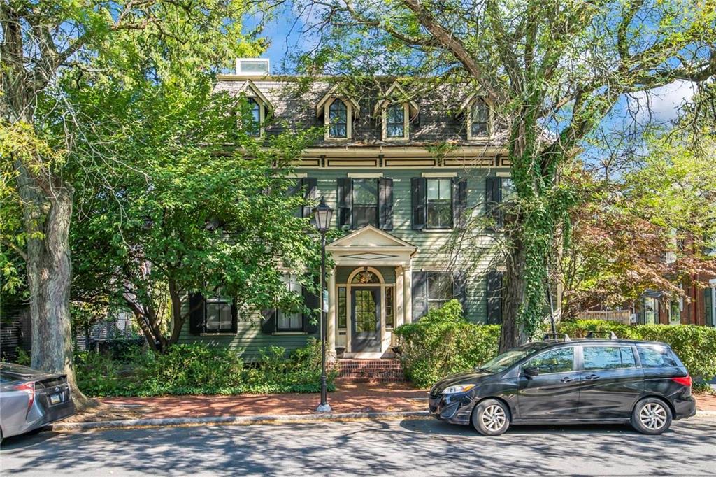 A green clapboard house with black shutters, Gothic-arched dormers and a pedimented entry portico