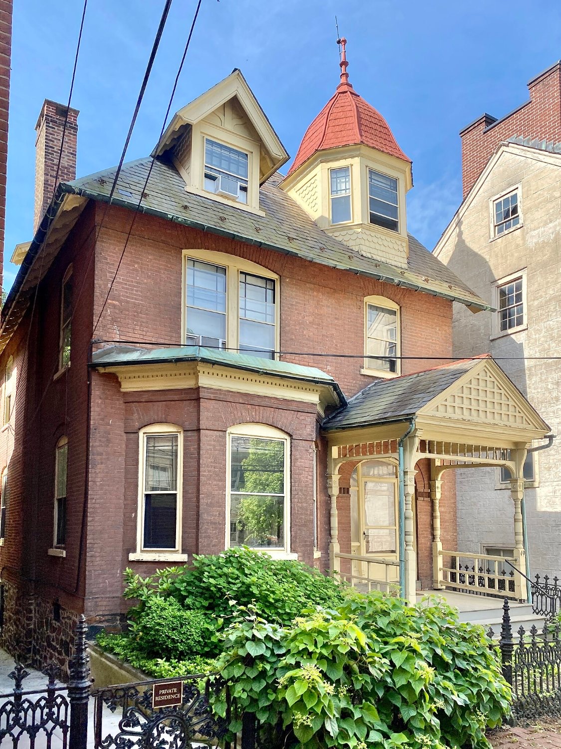 A brick Victorian house with a red conical turret roof and a small plaque on the iron fence reading Private Residence