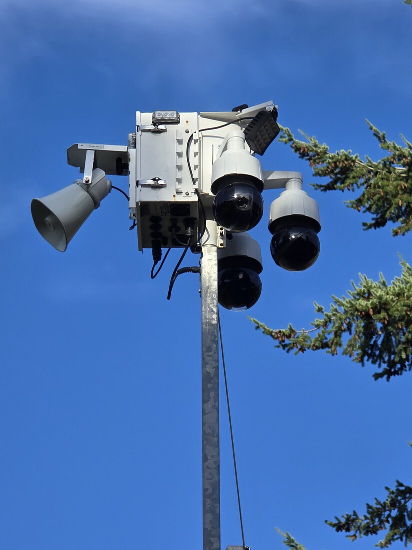 A cluster of surveillance cameras on a pole against a blue sky