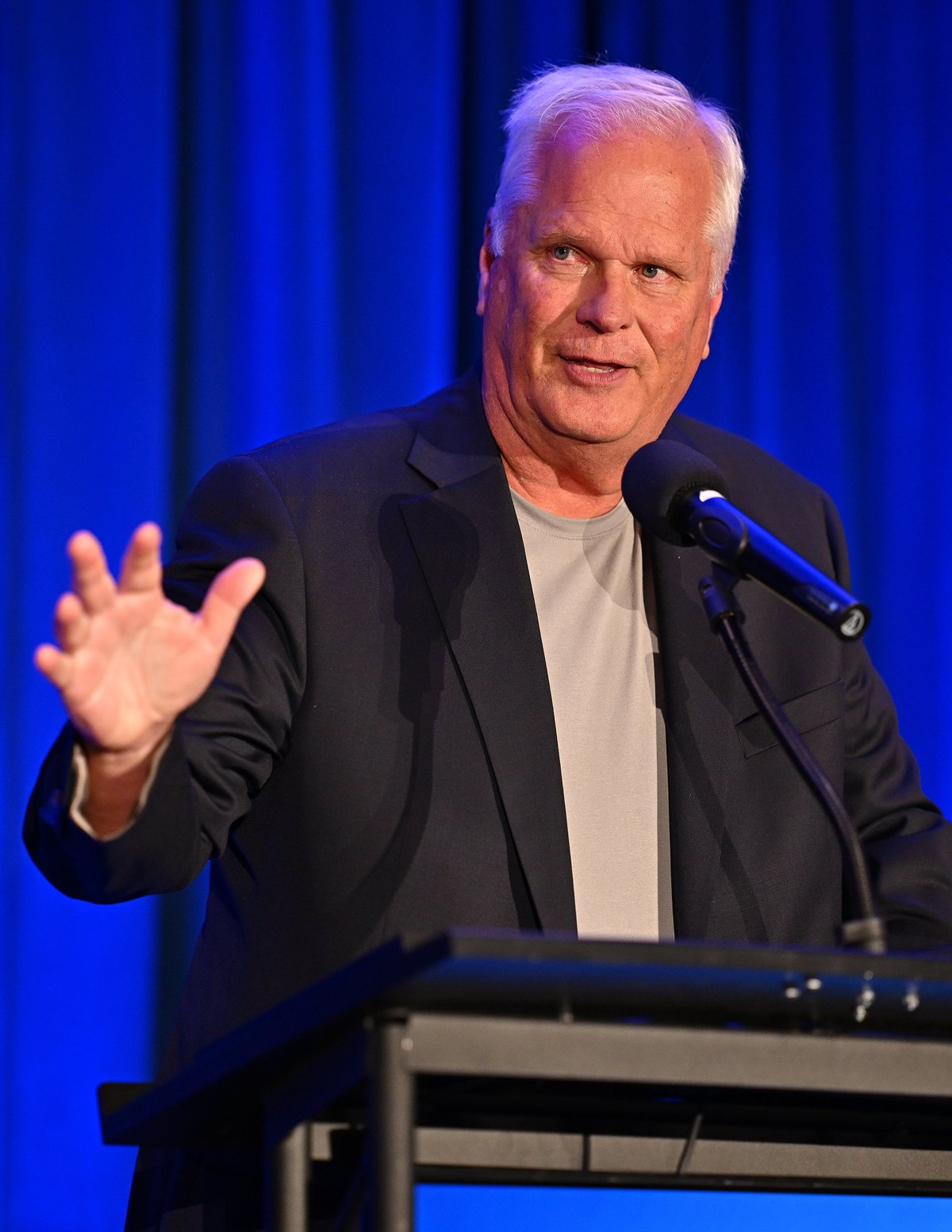 Tim Neiman speaking at a podium in front of a blue curtain