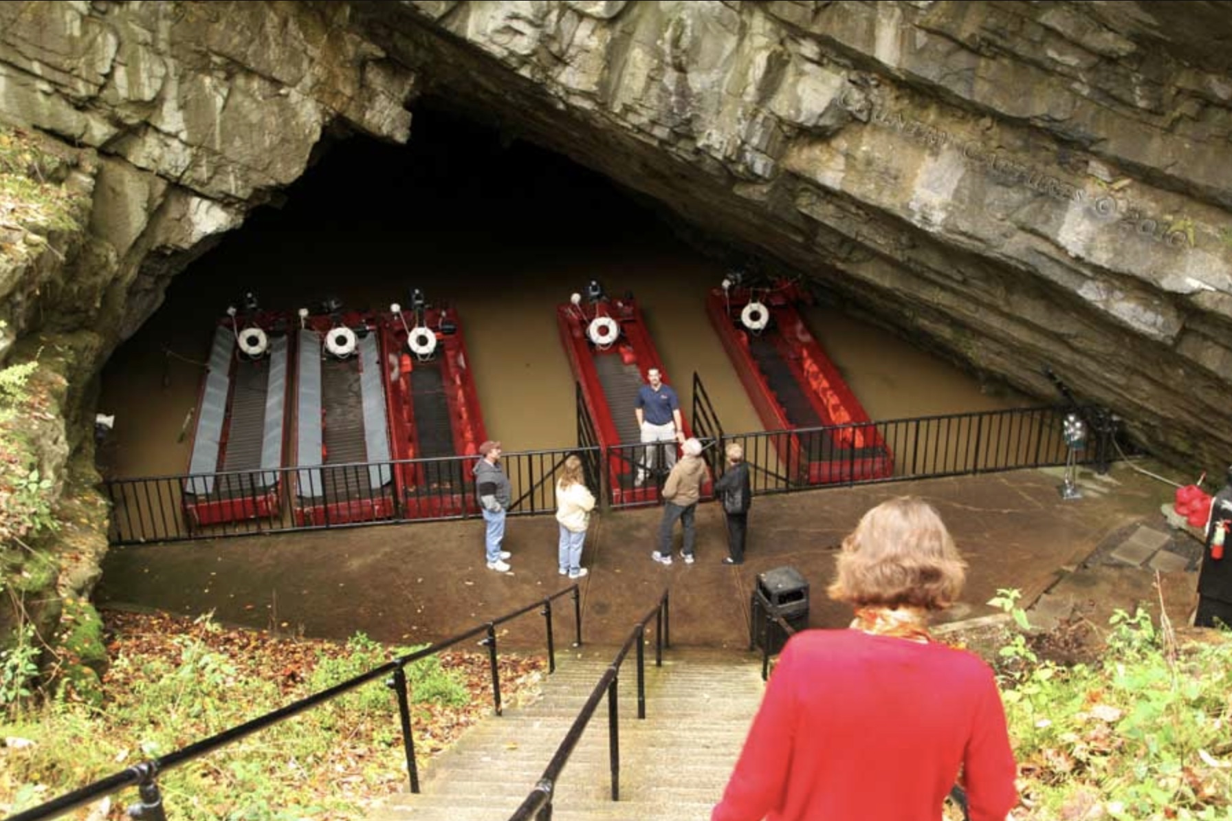Red flat-bottom tour boats docked at the mouth of Penn’s Cave, with visitors at the bottom of the stairs