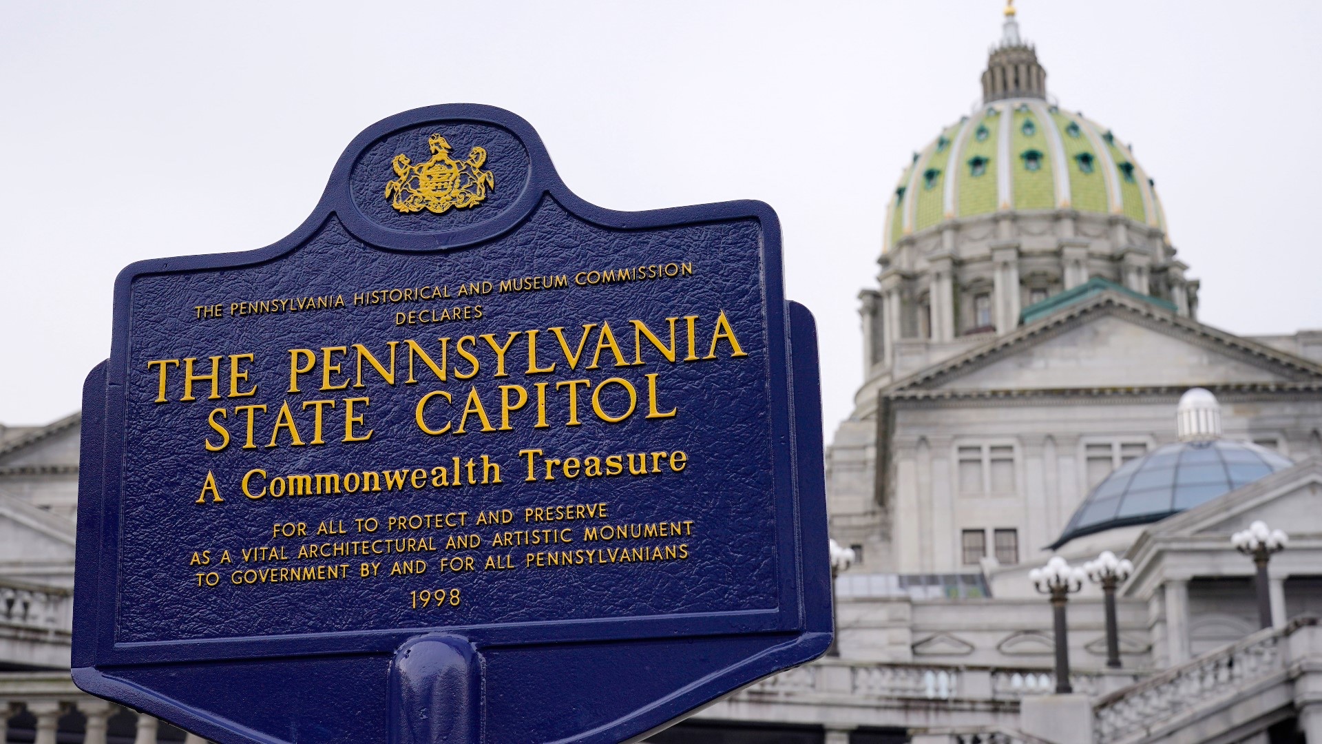 A historical marker outside the Pennsylvania State Capitol in Harrisburg, with the Capitol dome behind it