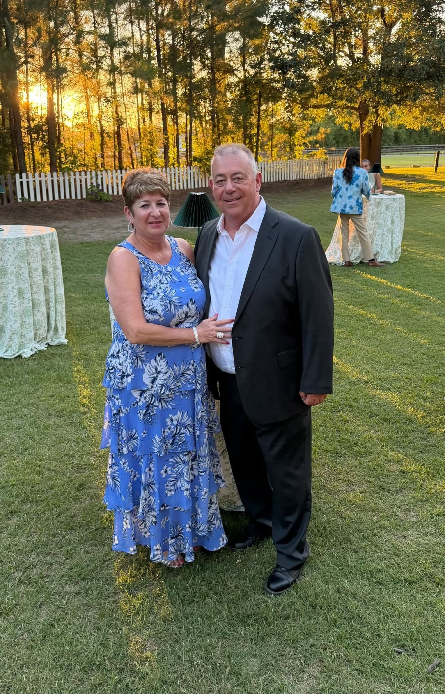 Ron and Sandy Serafin dressed for a wedding, standing on a lawn at sunset
