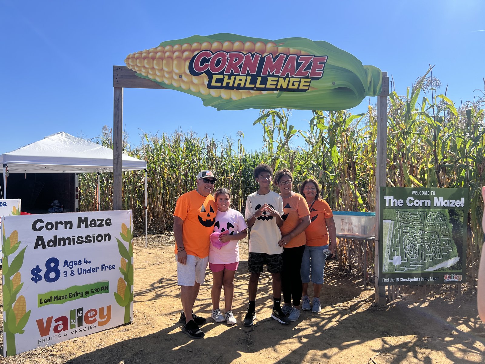 A family poses under the Corn Maze Challenge sign beside an admission board